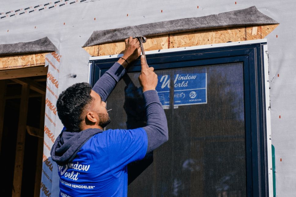 Window World worker installing a window with a hammer and nails.